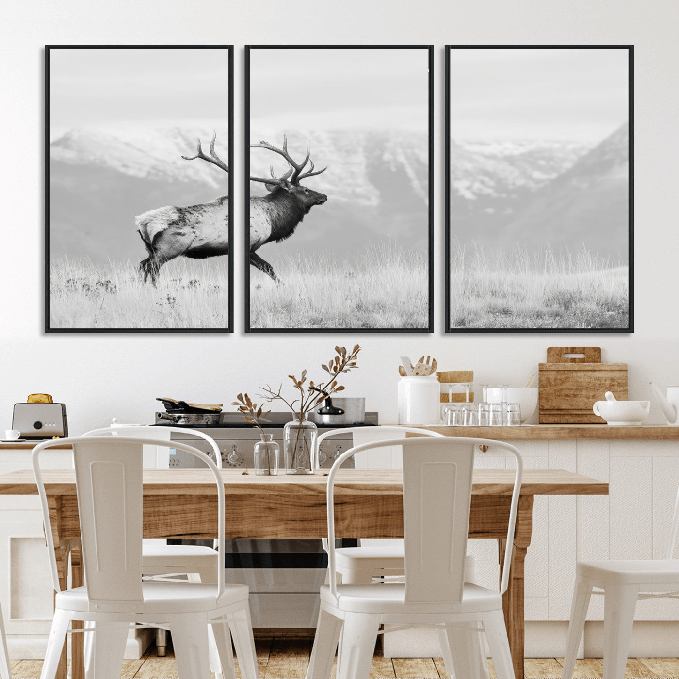 Black and white photograph of a majestic elk standing in a grassy field with snow-capped mountains in the background, creating a bold and rustic wilderness scene.