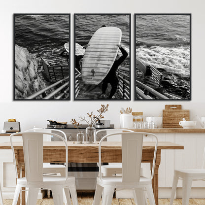 Black and white photo of surfers carrying boards down a rugged cliffside stairway, capturing a bold and adventurous coastal scene.