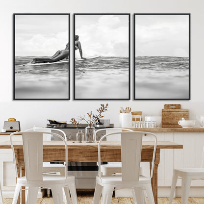A black and white ocean scene featuring a surfer girl waiting on her board, gazing at the horizon, capturing a tranquil and adventurous coastal moment.