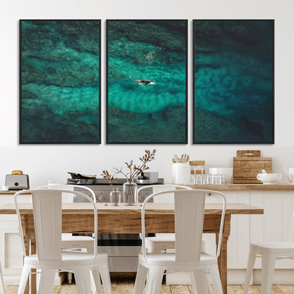An aerial view of a solo surfer paddling through crystal-clear turquoise waters over a sunlit reef, capturing the beauty and serenity of open water surfing.