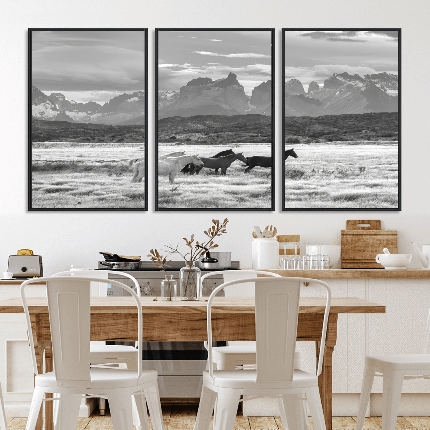 A black and white landscape of wild horses grazing in a vast grassland with towering mountains in the background, creating a moody and rustic western aesthetic.