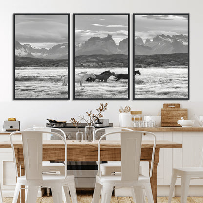 A black and white landscape of wild horses grazing in a vast grassland with towering mountains in the background, creating a moody and rustic western aesthetic.