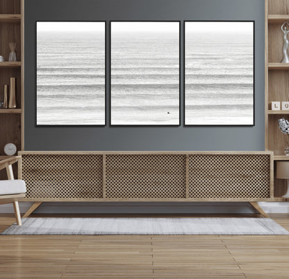 Monochrome photo of a lone surfer in calm layered waves, perfect for minimalist coastal or moody ocean-inspired wall decoration.