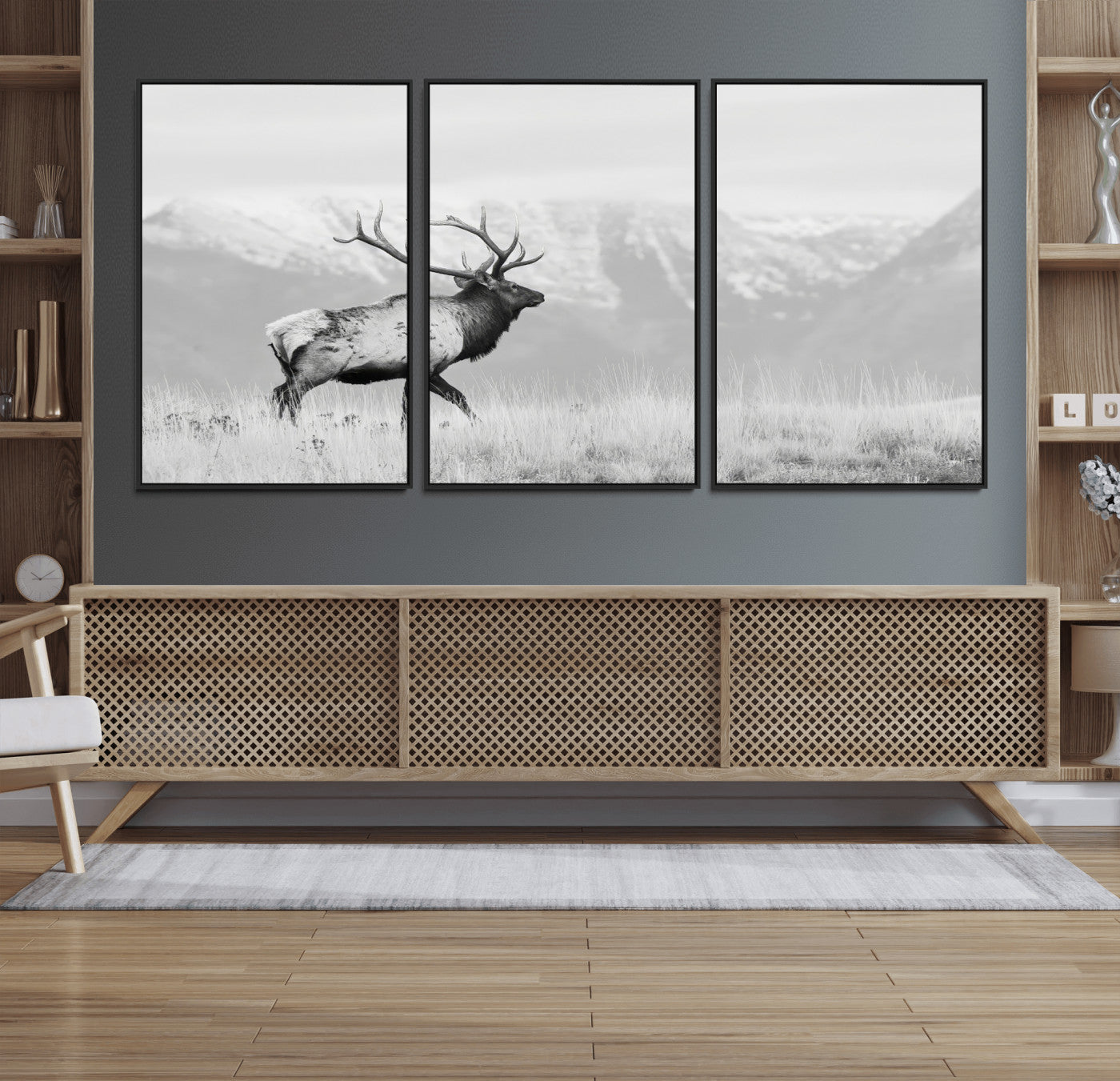 Black and white photograph of a majestic elk standing in a grassy field with snow-capped mountains in the background, creating a bold and rustic wilderness scene.