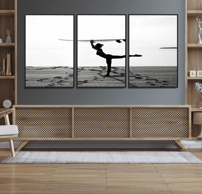 A woman balances a surfboard on her head while striking a yoga pose on the beach, silhouetted against a calm ocean horizon.