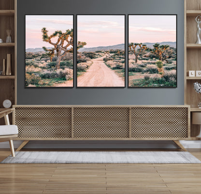 A dusty road winding through Joshua Tree National Park, framed by iconic twisted trees and warm desert tones under a soft pastel sky.