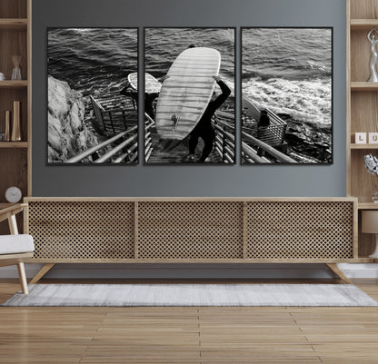 Black and white photo of surfers carrying boards down a rugged cliffside stairway, capturing a bold and adventurous coastal scene.
