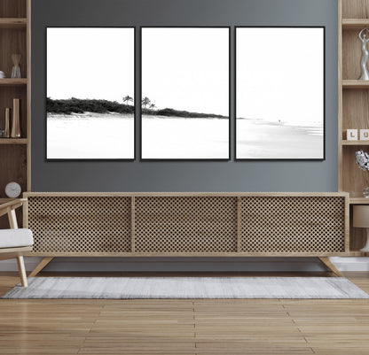 A black and white minimalist coastal scene with a vast open beach, distant palm trees, and a lone figure walking along the shoreline, evoking serenity and solitude.