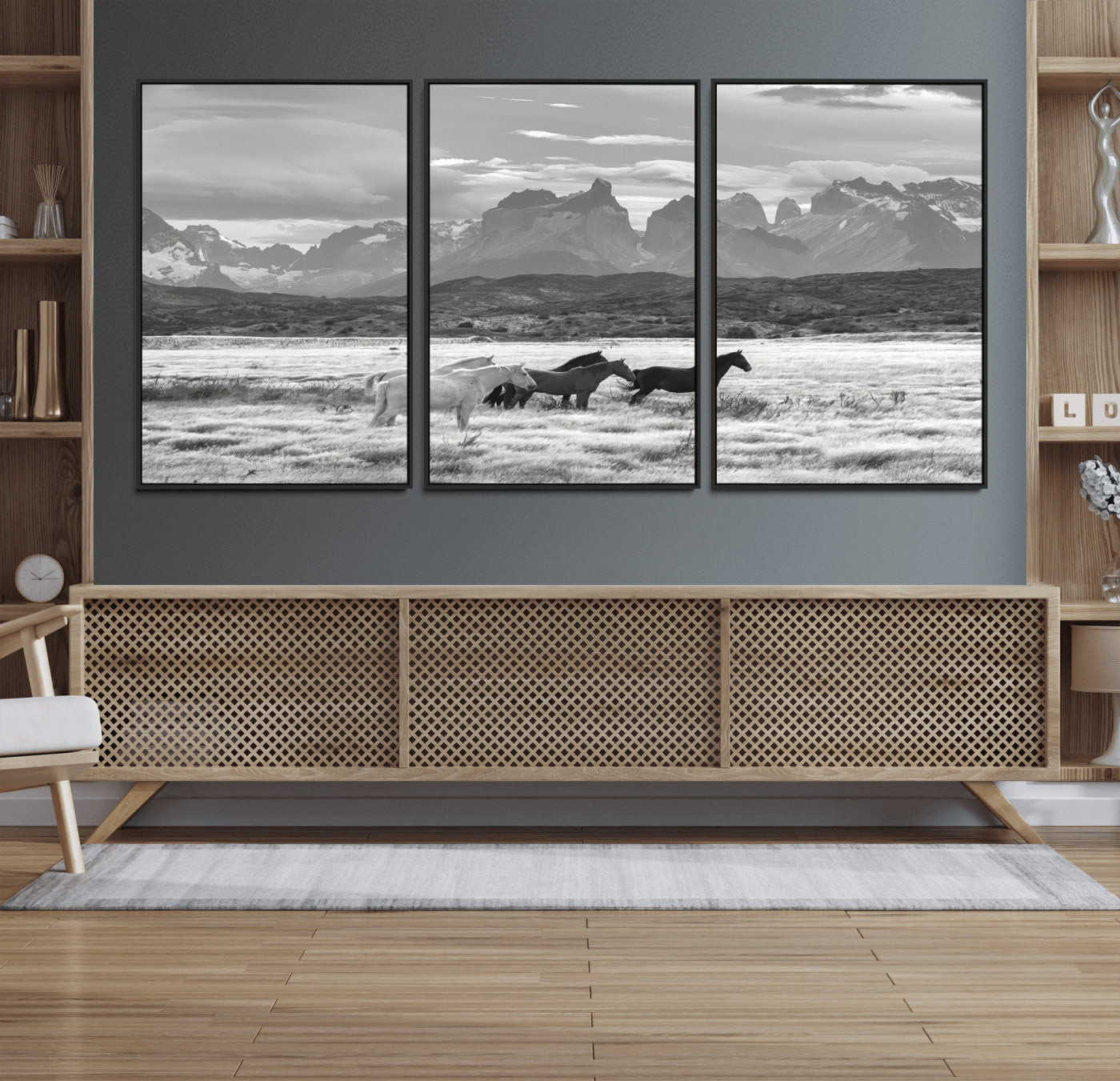 A black and white landscape of wild horses grazing in a vast grassland with towering mountains in the background, creating a moody and rustic western aesthetic.
