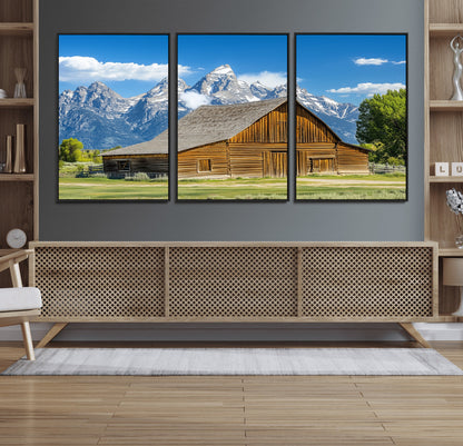 A rustic wooden barn sits in front of towering mountain peaks under a clear blue sky, perfect for farmhouse or cabin style interiors.