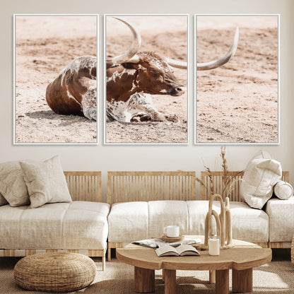Texas Longhorn bull resting on dusty ground with warm tones, ideal for rustic western or farmhouse-themed wall decor.