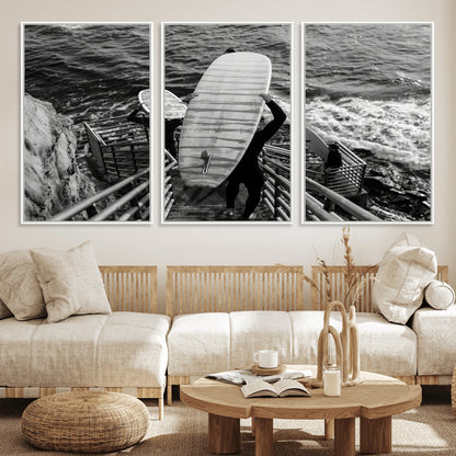 Black and white photo of surfers carrying boards down a rugged cliffside stairway, capturing a bold and adventurous coastal scene.