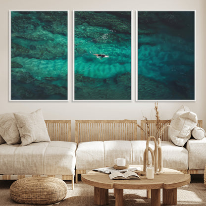 An aerial view of a solo surfer paddling through crystal-clear turquoise waters over a sunlit reef, capturing the beauty and serenity of open water surfing.