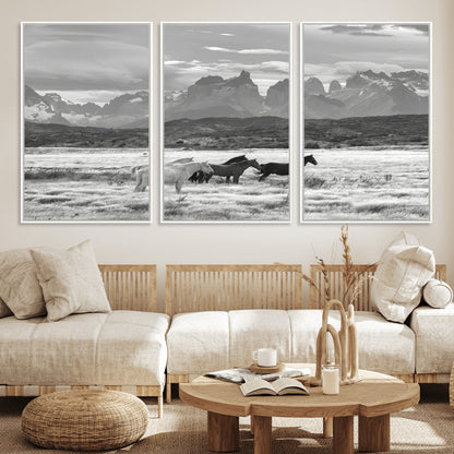 A black and white landscape of wild horses grazing in a vast grassland with towering mountains in the background, creating a moody and rustic western aesthetic.
