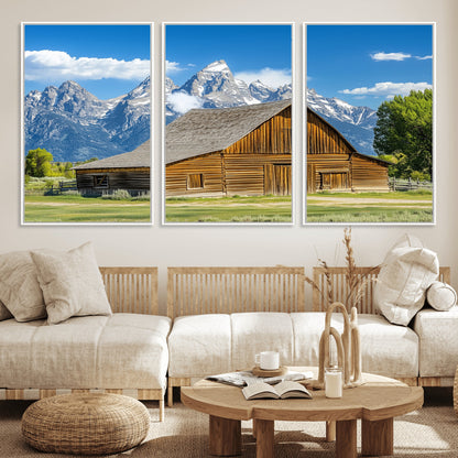 A rustic wooden barn sits in front of towering mountain peaks under a clear blue sky, perfect for farmhouse or cabin style interiors.