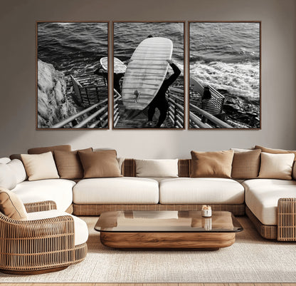 Black and white photo of surfers carrying boards down a rugged cliffside stairway, capturing a bold and adventurous coastal scene.