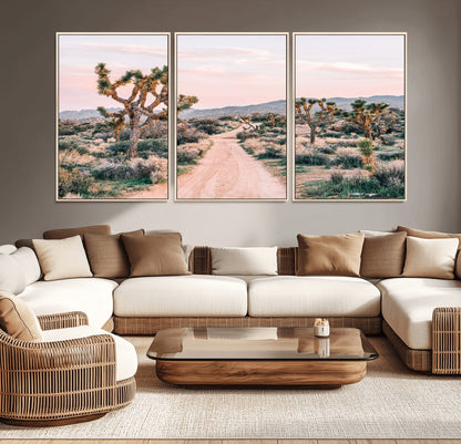 A dusty road winding through Joshua Tree National Park, framed by iconic twisted trees and warm desert tones under a soft pastel sky.