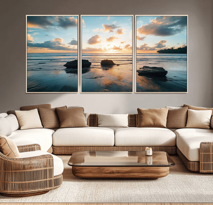 A serene beach at sunset with vibrant clouds, calm water, and rocks in the foreground reflecting the warm colors of the setting sun.
