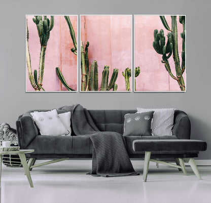 Framed canvas of tall green cacti against a soft pink wall, ideal for modern desert or colorful southwest-inspired home decor.