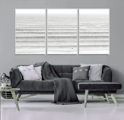 Monochrome photo of a lone surfer in calm layered waves, perfect for minimalist coastal or moody ocean-inspired wall decoration.