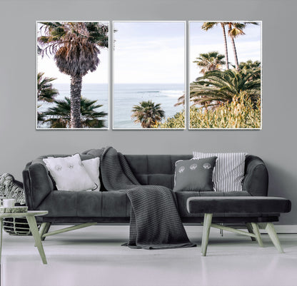 Scenic coastal view with tall palm trees overlooking a calm ocean, soft blue waves, and surfers in the distance, creating a peaceful tropical vibe.