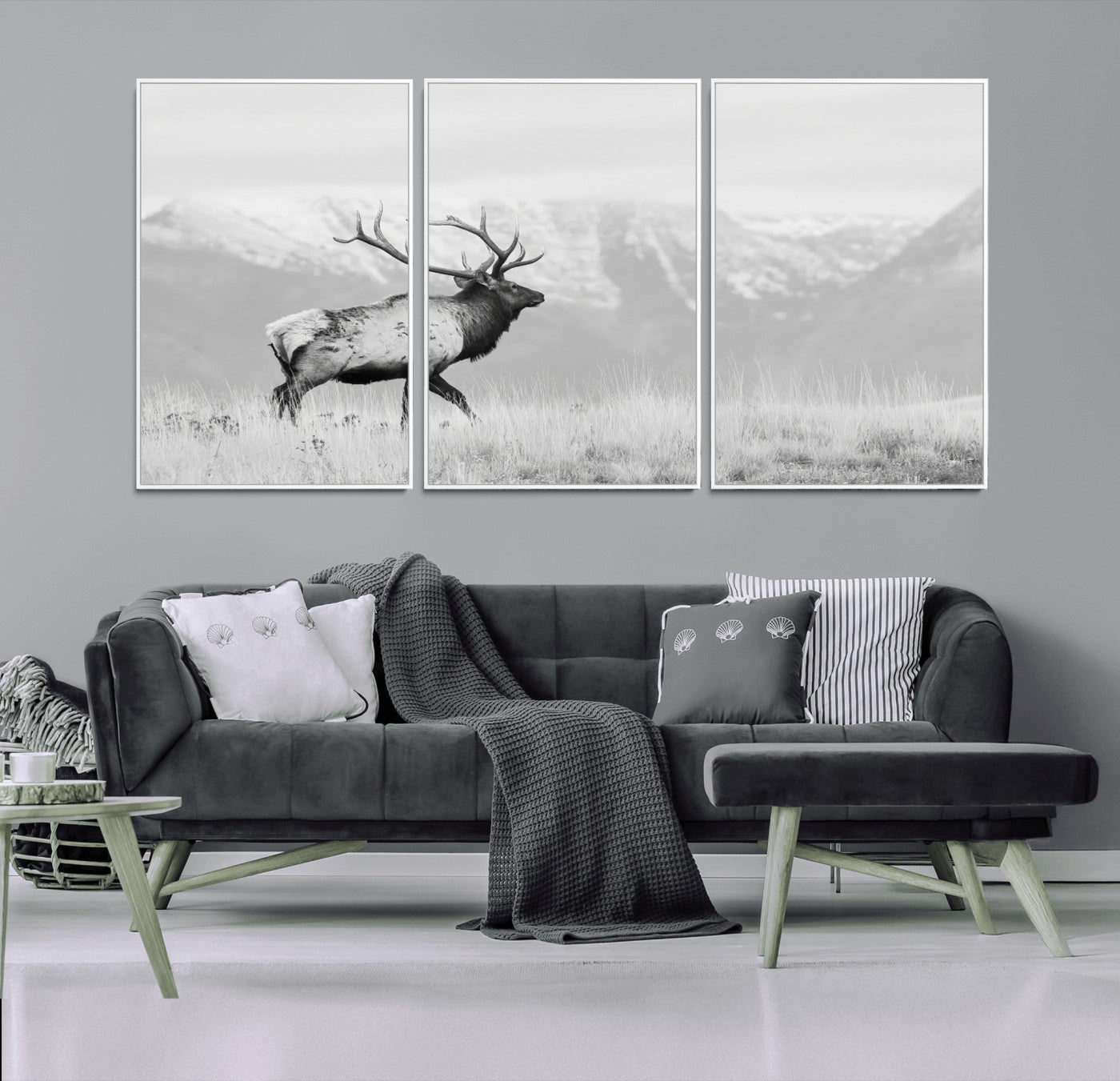 Black and white photograph of a majestic elk standing in a grassy field with snow-capped mountains in the background, creating a bold and rustic wilderness scene.