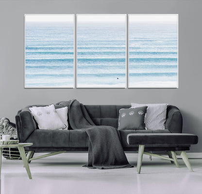 Minimalist ocean view with soft blue waves and a lone surfer, creating a serene and airy coastal aesthetic, perfect for tranquil home decor.