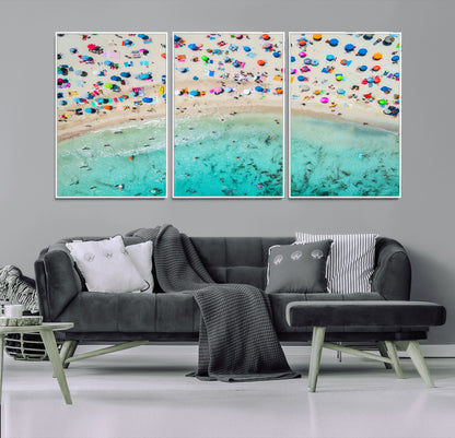Aerial view of a vibrant beach filled with colorful umbrellas and people enjoying the turquoise ocean, capturing a lively summer vacation scene.