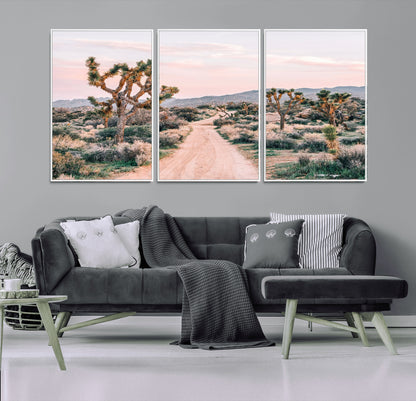 A dusty road winding through Joshua Tree National Park, framed by iconic twisted trees and warm desert tones under a soft pastel sky.