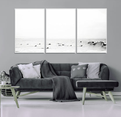 A group of surfers floating in the ocean, waiting for waves under a vast, moody sky, captured in black and white.