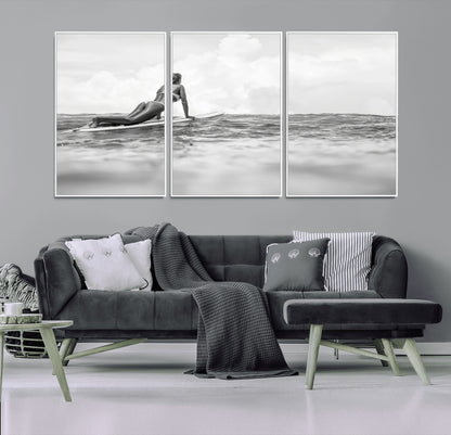 A black and white ocean scene featuring a surfer girl waiting on her board, gazing at the horizon, capturing a tranquil and adventurous coastal moment.
