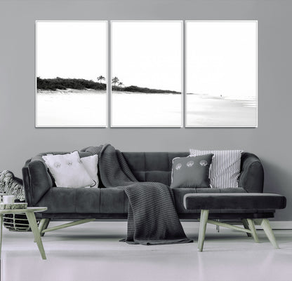 A black and white minimalist coastal scene with a vast open beach, distant palm trees, and a lone figure walking along the shoreline, evoking serenity and solitude.