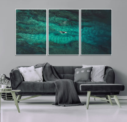 An aerial view of a solo surfer paddling through crystal-clear turquoise waters over a sunlit reef, capturing the beauty and serenity of open water surfing.