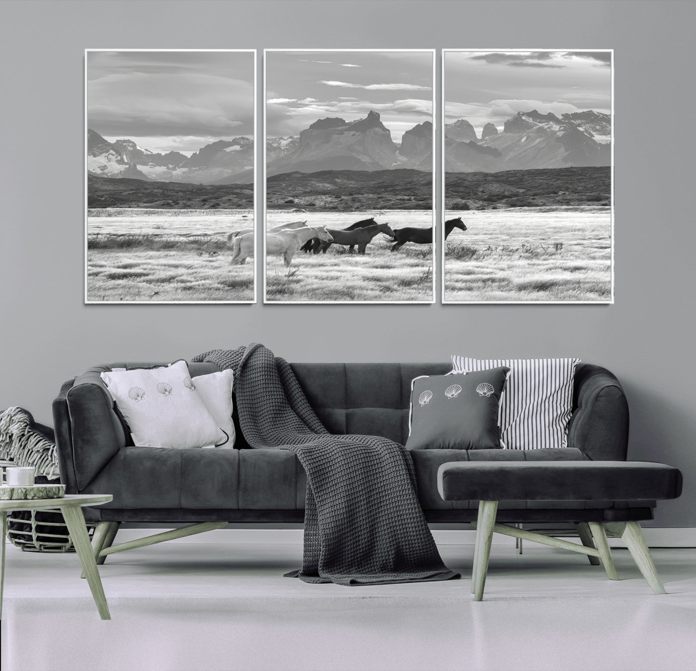 A black and white landscape of wild horses grazing in a vast grassland with towering mountains in the background, creating a moody and rustic western aesthetic.