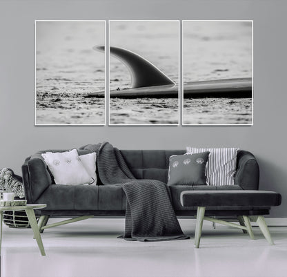 A black and white close-up of a surfboard fin resting on the sandy shore, highlighting minimalist beach aesthetics and classic surf culture.