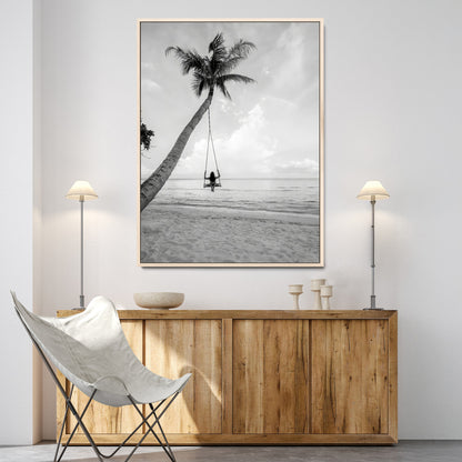 Monochrome photo of a woman swinging from a palm tree on a serene beach, ideal for minimalist or tropical coastal decor.