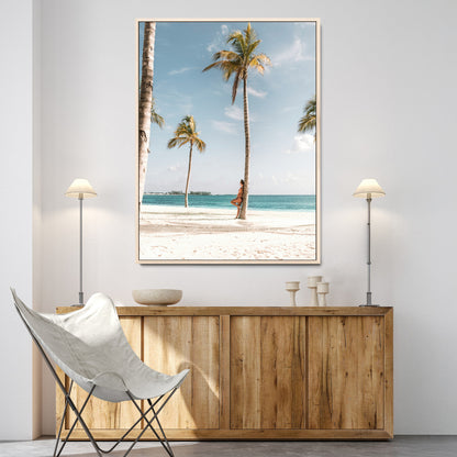 Person leaning on a palm tree at a tropical beach with white sand and turquoise water, perfect for coastal or beach-themed home decor.