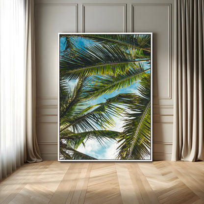 Looking up at lush green palm leaves against a bright blue sky, creating a tropical and relaxing coastal aesthetic.