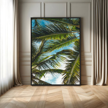 Looking up at lush green palm leaves against a bright blue sky, creating a tropical and relaxing coastal aesthetic.