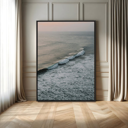 Aerial view of ocean waves rolling towards the shore under a soft sunset sky, creating a peaceful and minimalist coastal scene.