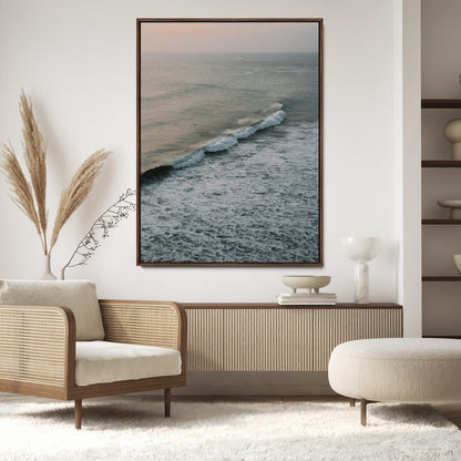 Aerial view of ocean waves rolling towards the shore under a soft sunset sky, creating a peaceful and minimalist coastal scene.