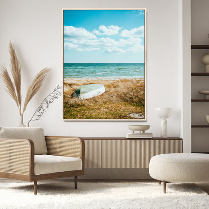 A small boat resting on a grassy shore with ocean waves and a bright blue sky, creating a peaceful coastal atmosphere.