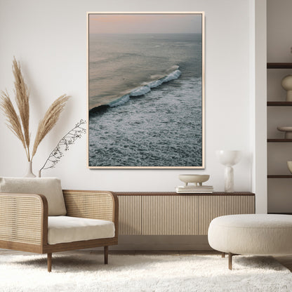 Aerial view of ocean waves rolling towards the shore under a soft sunset sky, creating a peaceful and minimalist coastal scene.