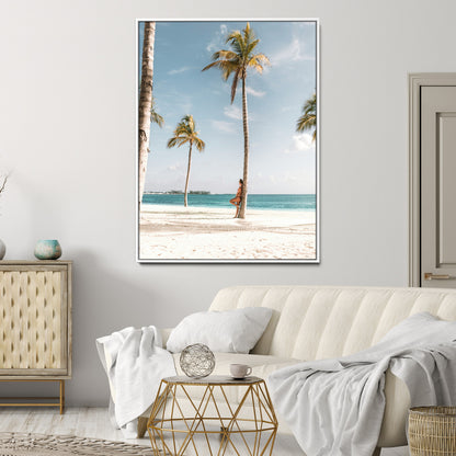 Person leaning on a palm tree at a tropical beach with white sand and turquoise water, perfect for coastal or beach-themed home decor.