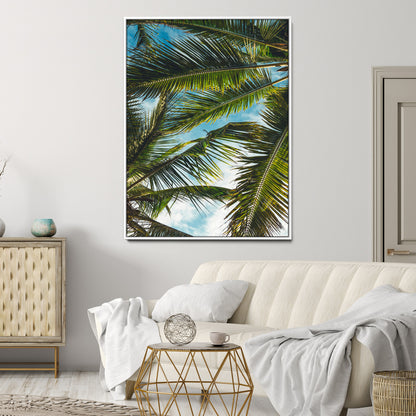 Looking up at lush green palm leaves against a bright blue sky, creating a tropical and relaxing coastal aesthetic.