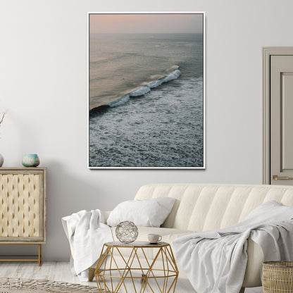 Aerial view of ocean waves rolling towards the shore under a soft sunset sky, creating a peaceful and minimalist coastal scene.