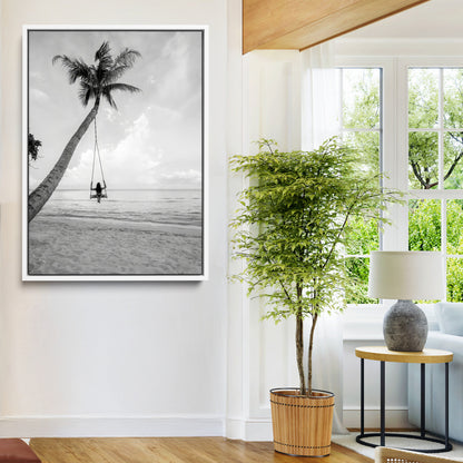 Monochrome photo of a woman swinging from a palm tree on a serene beach, ideal for minimalist or tropical coastal decor.