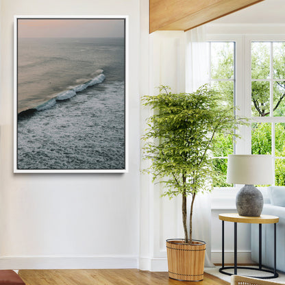 Aerial view of ocean waves rolling towards the shore under a soft sunset sky, creating a peaceful and minimalist coastal scene.