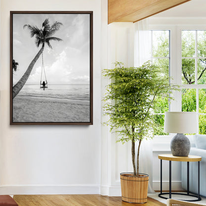 Monochrome photo of a woman swinging from a palm tree on a serene beach, ideal for minimalist or tropical coastal decor.