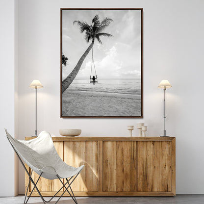 Monochrome photo of a woman swinging from a palm tree on a serene beach, ideal for minimalist or tropical coastal decor.